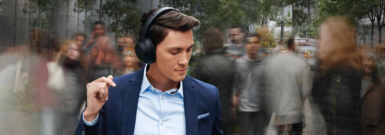  A male wearing the Sony WH-1000XM3 Headphones are dancing in crowded street, with background street and people blurred 